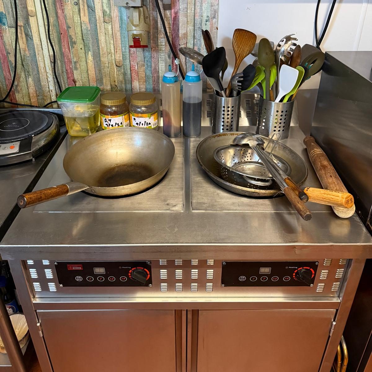 Commercial Cleaning – Restaurant | After Photo Stainless steel countertop with two cooking pans and multiple utensils on storage racks.