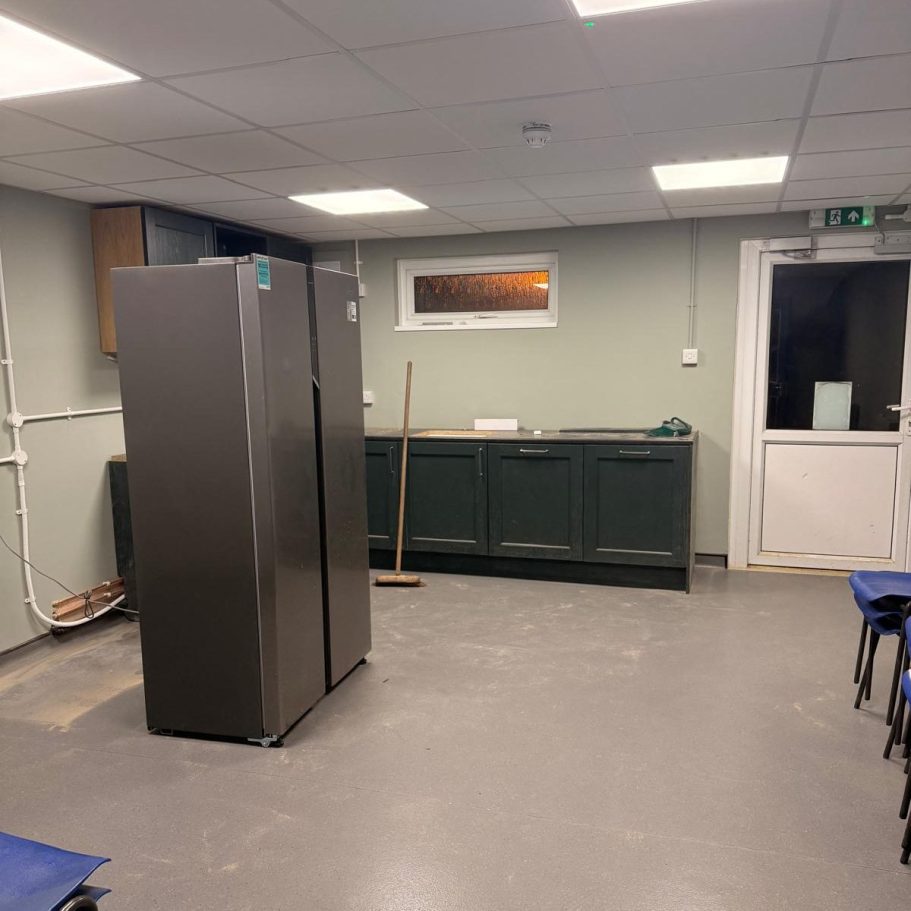 Commercial Cleaning – Industrial | Before Photo | Kitchen View of a minimalist kitchen with a tall fridge, sink, and seating area.